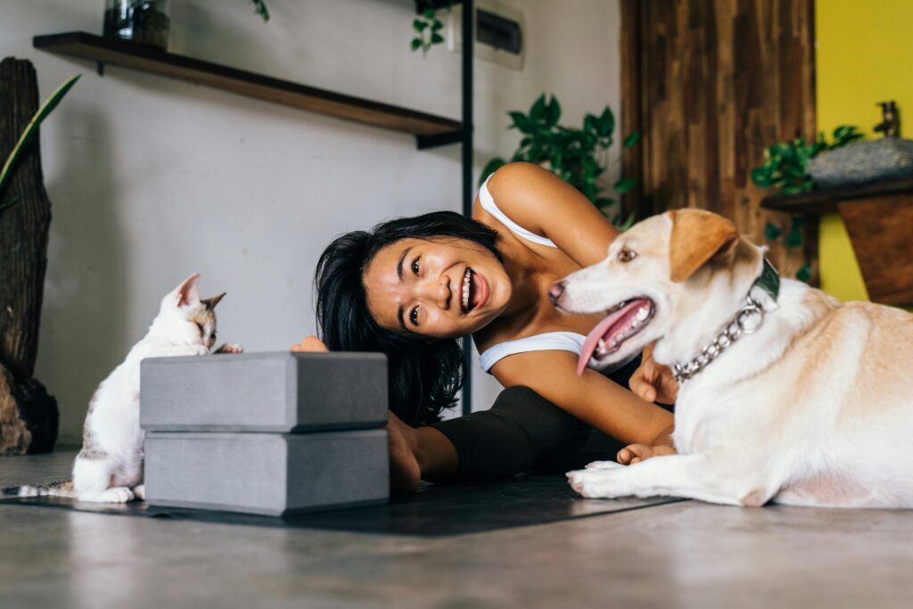 Smiling woman practicing yoga indoors with her dog and cat, embracing a healthy lifestyle.