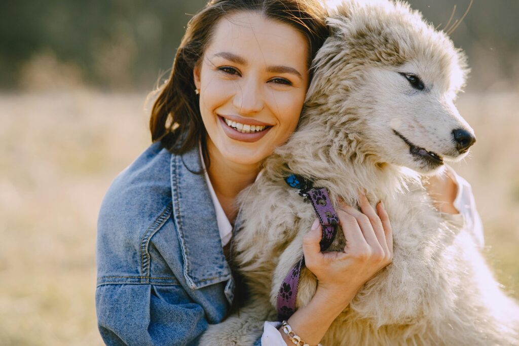 Joyful woman in a denim jacket hugging a fluffy dog outdoors, showcasing friendship and happiness.